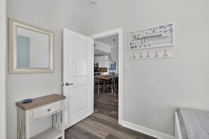 A hallway with a white door, a mirror, a small table, and a sign that reads 'Happiness is a day at the beach.' - Bring the Whole Crew Sleeps 13 MerSea (Bolivar Peninsula)