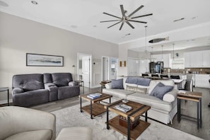 A modern living room with a grey sofa, a white sofa, and a coffee table. There is a kitchen area with white cabinets and a dining table. - Bring the Whole Crew Sleeps 13 MerSea (Bolivar Peninsula)