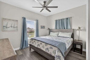 Une chambre à coucher avec un lit, un ventilateur de plafond, une table de chevet, une lampe et une fenêtre avec des rideaux.