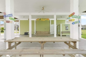 A covered outdoor area with a wooden bench, a ceiling fan, and signs pointing to various destinations. - Bring the Whole Crew Sleeps 13 MerSea (Bolivar Peninsula)