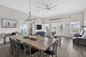 A spacious living area with a large wooden dining table, comfortable seating, a television, and a view of the outdoors. - Bring the Whole Crew Sleeps 13 MerSea (Bolivar Peninsula)