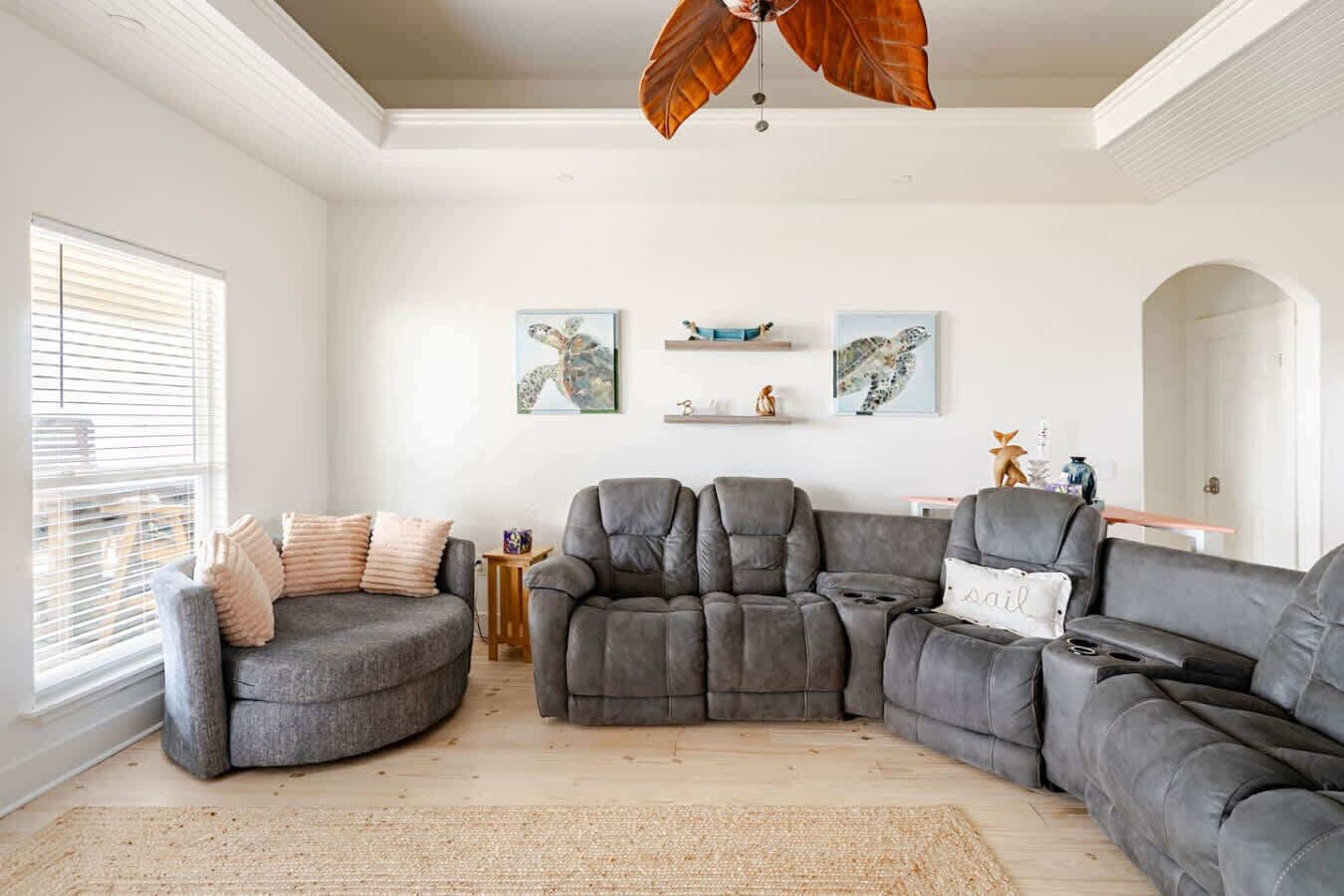 Una sala de estar moderna con un sofá seccional, un sillón reclinable y una mesa de centro. Hay dos estantes montados en la pared con objetos decorativos.