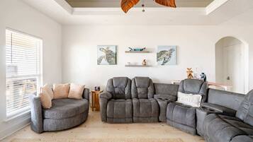 Una sala de estar moderna con un sofá seccional, un sillón reclinable y una mesa de centro. Hay dos estantes montados en la pared con objetos decorativos.