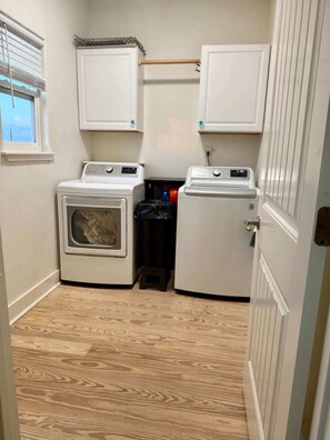 A laundry room with two washing machines, a dryer, and a small trash bin. - Beachfront Fire Pit  Gourmet Kitchen Views (Bolivar Peninsula)