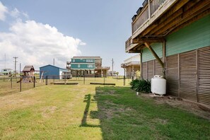 A fenced yard with a swing set, a building with a green roof, and a large water tank. - Beachfront Fire Pit  Gourmet Kitchen Views (Bolivar Peninsula)