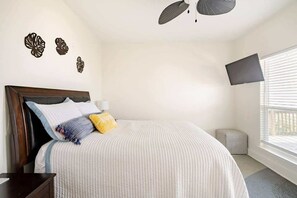 A bedroom with a bed, bedside table, wall-mounted TV, and decorative wall art. - Beachfront Fire Pit  Gourmet Kitchen Views (Bolivar Peninsula)