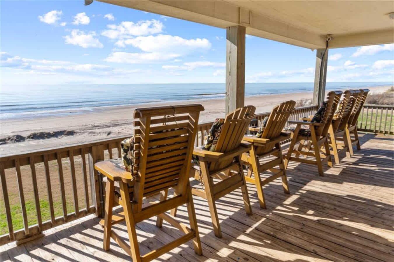 Terraza de madera con sillas Adirondack mirando a la playa.
