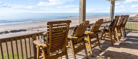 Um deck de madeira com cadeiras Adirondack voltadas para a praia.