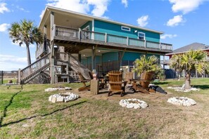 A two-story house with a balcony, outdoor furniture, and palm trees. - Beachfront Fire Pit  Gourmet Kitchen Views (Bolivar Peninsula)