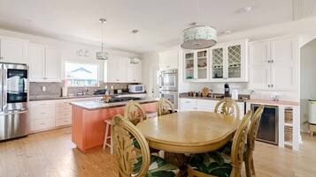 Una cocina amplia con armarios blancos, una isla central y un comedor con mesa y sillas de madera.