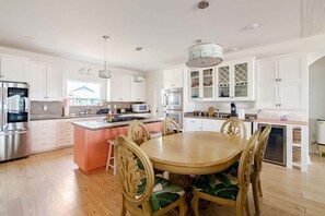 A spacious kitchen with white cabinets, a central island, and a dining area with a wooden table and chairs. - Beachfront Fire Pit  Gourmet Kitchen Views (Bolivar Peninsula)