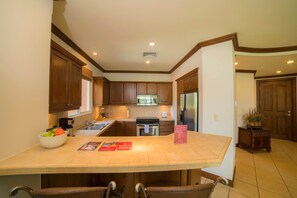 A kitchen with wooden cabinets, a stainless steel refrigerator, a built-in oven, and a large island with bar stools. - Bay Residence 8C 3 bdr 2 bath (Herradura)