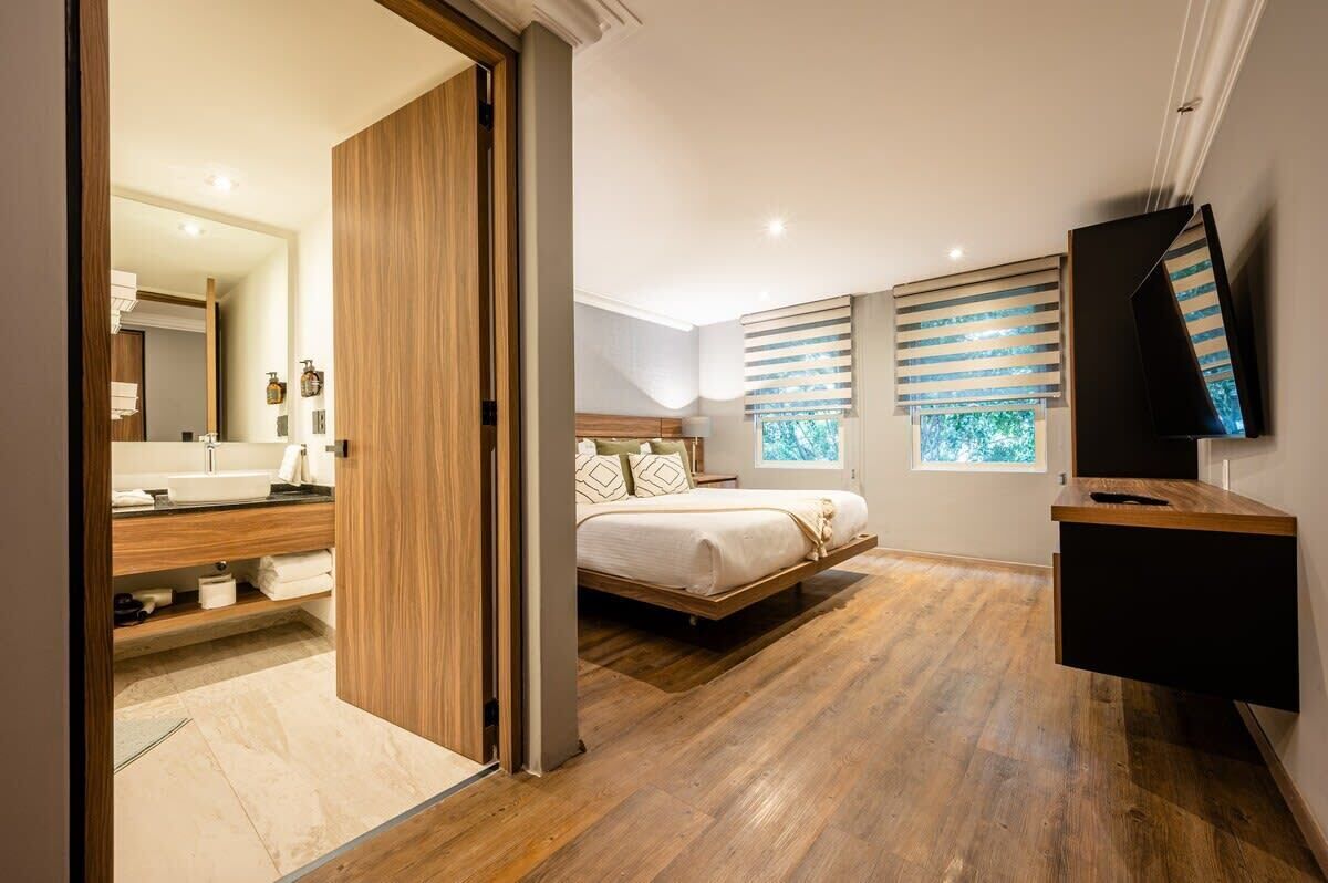 Ein modernes Schlafzimmer mit Holzboden, einem Bett mit Kopfteil, einem Fernseher und einem Fenster mit Jalousien.