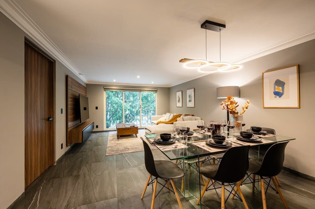 Un espace repas moderne avec une table en verre, des chaises noires et un lustre.
