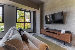 A modern living room with a large window, a sofa, a flat-screen TV mounted on a wall, and a wooden console table. - Capitalia ,Terrace, Rooftop Jacuzzi, Gym & more (Ciudad de México)