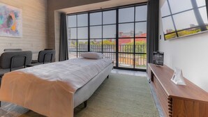 Camera d'albergo moderna con un letto grande, una scrivania con sedie, un comodino in legno e vista panoramica attraverso ampie finestre.