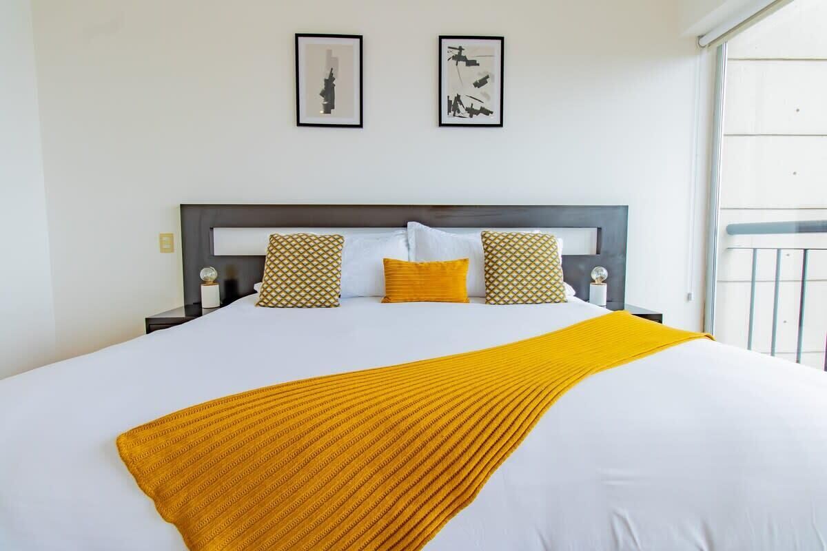 Un lit recouvert d’une couvre-lit blanche et jaune, agrémenté de deux coussins à motifs et d’un plaid jaune.