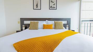 Un lit recouvert d’une couvre-lit blanche et jaune, agrémenté de deux coussins à motifs et d’un plaid jaune.
