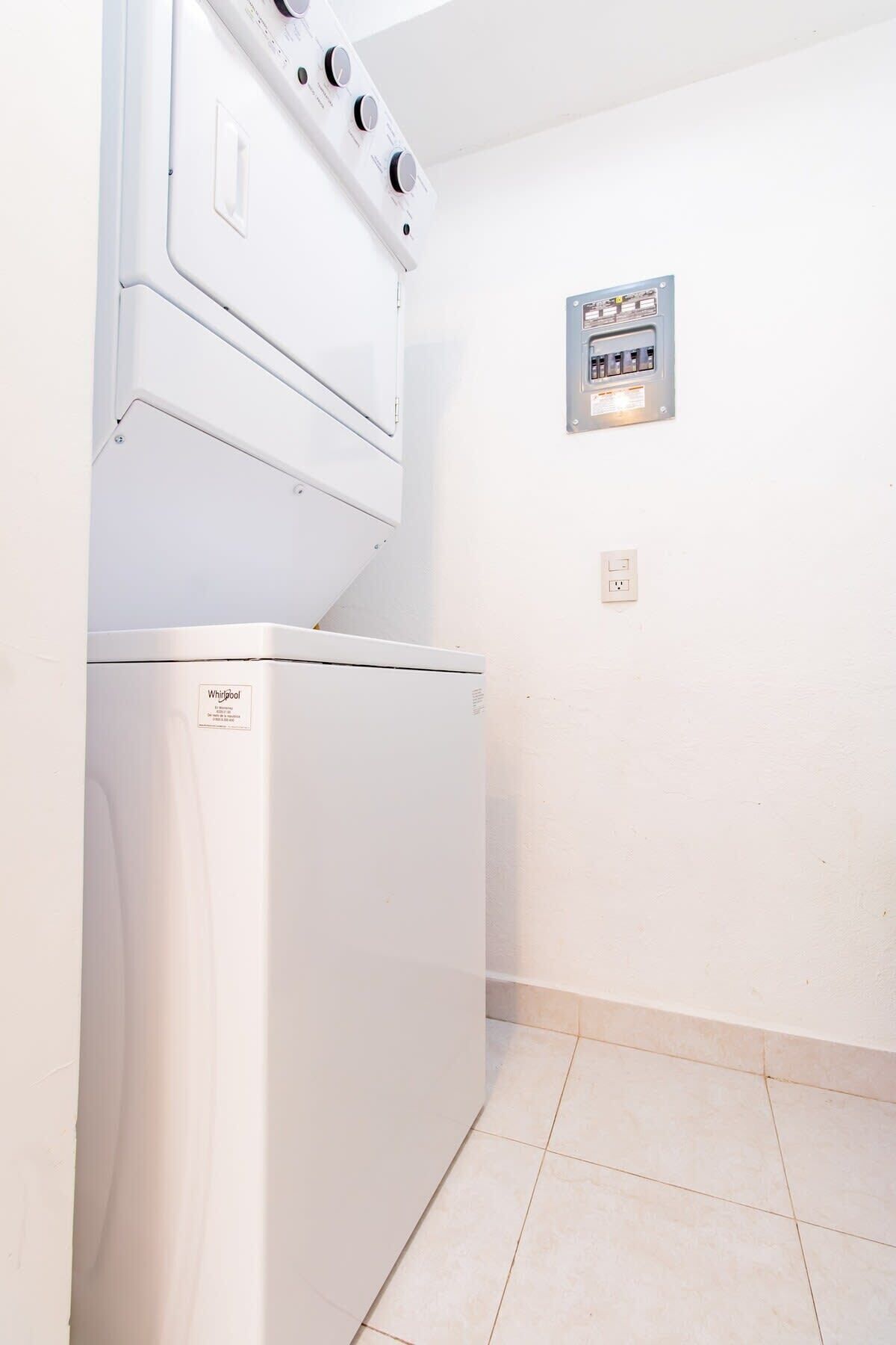 Une petite buanderie équipée d’un lave-linge et d’un sèche-linge Whirlpool, d’un panneau de commande et d’une prise électrique murale.
