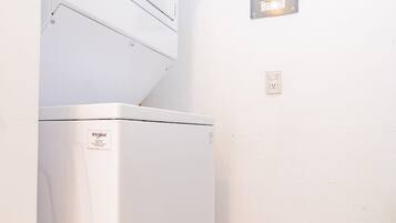Une petite buanderie équipée d’un lave-linge et d’un sèche-linge Whirlpool, d’un panneau de commande et d’une prise électrique murale.