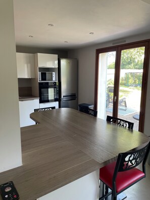 Eine moderne Küche mit großem Esstisch, integrierten Geräten und einer Schiebeglasdoor zu einer Terrasse.