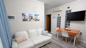 En moderne stue med en sofa, et spisebord med stole, et fladskærms-tv på væggen og et sæt billeder over sofaen.