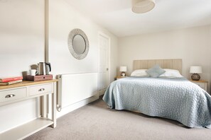 Ein Schlafzimmer mit Bett, Nachttischen, Kommode, Heizkörper und Spiegel an der Wand.