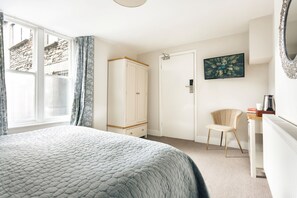 Ein Schlafzimmer mit einem Bett, einem Kleiderschrank, einem Schreibtisch mit Stuhl, einem Fernseher und einem Bild an der Wand.