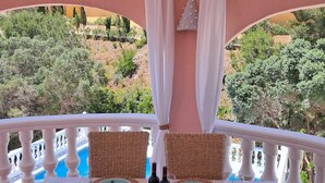 A dining area with wicker chairs, a table set for two, and a view of a pool and greenery. - Villa in Cumbre del Sol—bookable for stays of 11 days or more (El Poble Nou de Benitatxell/Benitachell)
