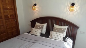 A bed with a wooden headboard, two wall-mounted lights, and a door with a wooden panel design. - Villa in Cumbre del Sol—bookable for stays of 11 days or more (El Poble Nou de Benitatxell/Benitachell)