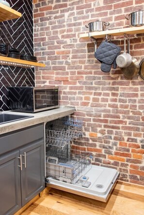 A kitchen with a dishwasher, a microwave, and a brick wall. - Artsy Apt in Lawrenceville with deck & parking (Pittsburgh)