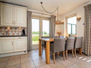 A kitchen with white cabinets, a dining table with chairs, and a view of the outdoors. - Pet-free Texel Villa With Sauna (De Koog)