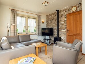 A living room with a sofa, a coffee table, a TV, and a fireplace. - Pet-free Texel Villa With Sauna (De Koog)