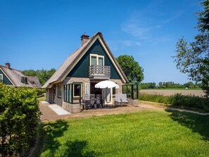 A traditional house with a thatched roof, a stone foundation, and a small patio with outdoor seating. - Pet-free Texel Villa With Sauna (De Koog)