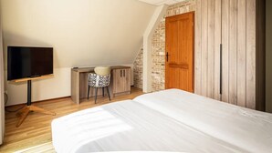 Quarto com cama, escrivaninha com cadeira, televisão e guarda-roupa de madeira.