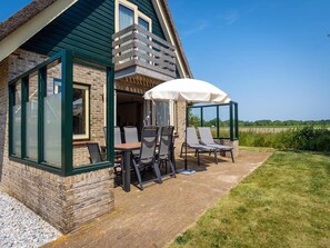 A house with a patio area featuring outdoor seating and a covered table. - Pet-free Texel Villa With Sauna (De Koog)