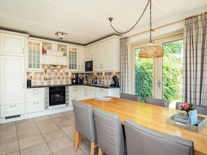 A modern kitchen with white cabinetry, a large island with seating, and a view of greenery outside. - Pet-free Texel Villa With Sauna (De Koog)