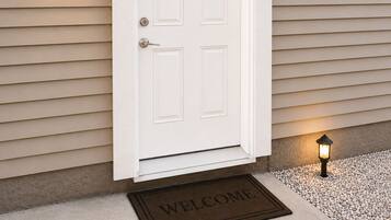 A white door with a doormat reading 'WELCOME' and two wall-mounted lanterns on either side.