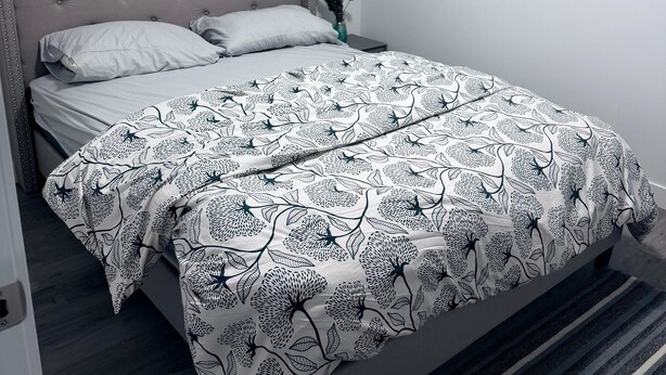 A bedroom with a bed, a window with blinds, a framed picture on the wall, and a bedside table with a vase. - Home away from home (Edmonton)