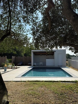 A swimming pool with a covered patio area, surrounded by a wooden fence and trees.