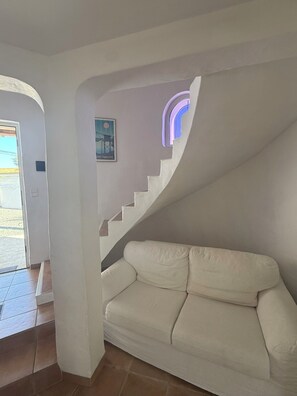 A white staircase leading to a landing with a white sofa and a framed picture on the wall.