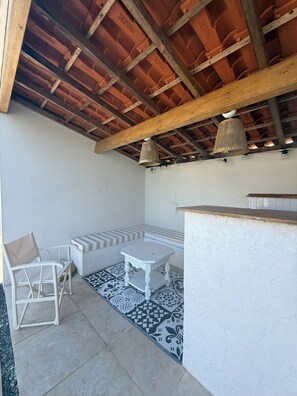 Un patio al aire libre con techo de madera, una mesa blanca, un banco y una silla.