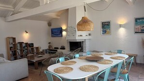 Een eetruimte met een ronde tafel, omringd door stoelen, een open haard en een plafond met zichtbare balken.