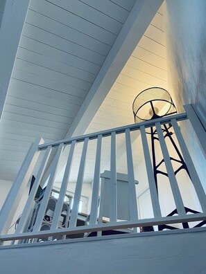 A white staircase with a metal railing, leading to a room with a ceiling fan and a window.