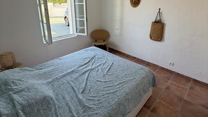 Een slaapkamer met een bed, een raam, een hanglamp en een stoel.