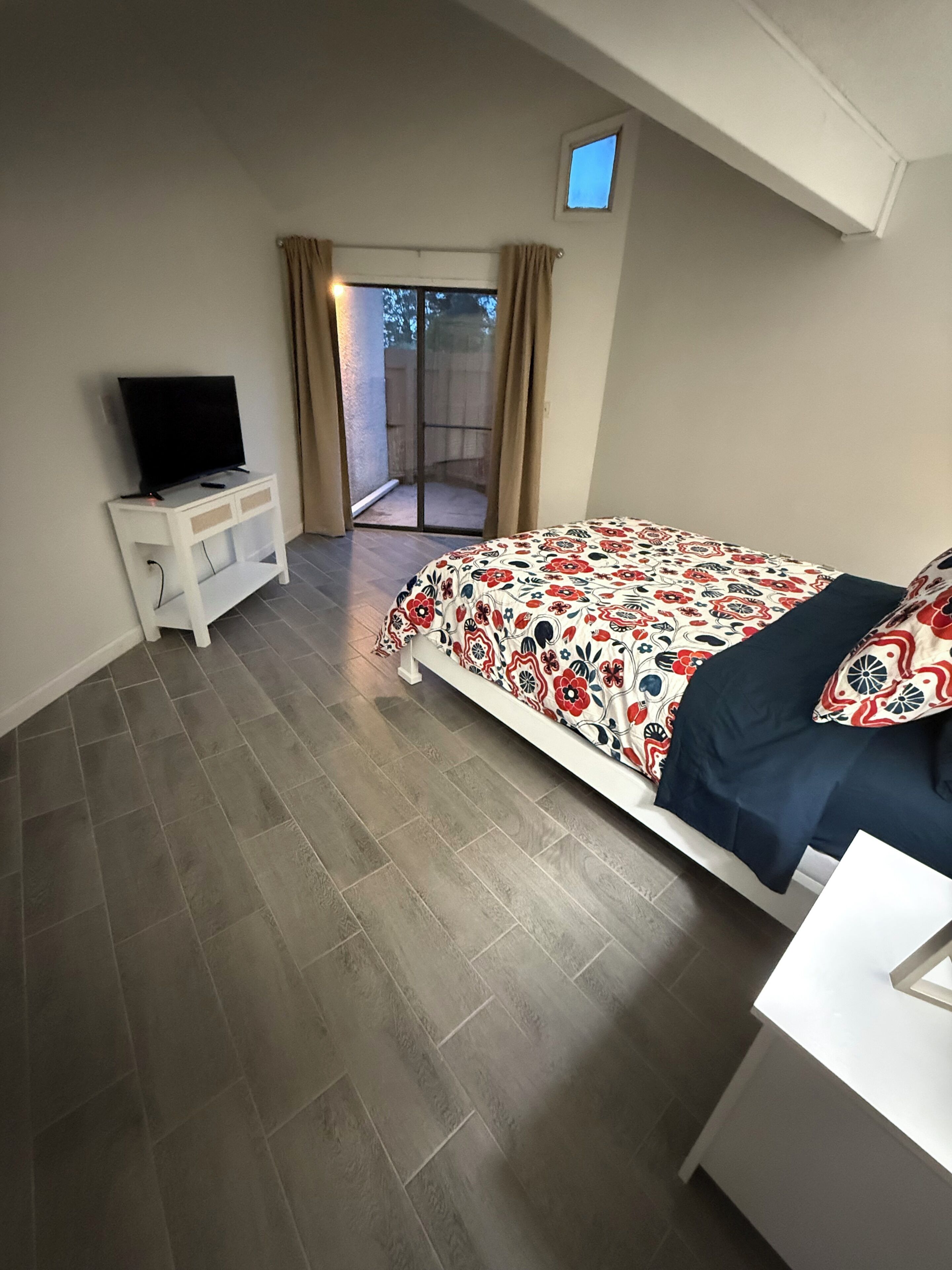 Ein Schlafzimmer mit einem Bett, einem Fernseher auf einem Nachttisch und einer Glastür, die zu einem Außenbereich führt.
