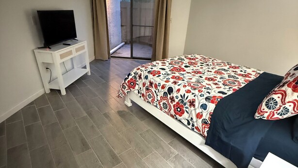 Una camera da letto con un letto, una TV su un comodino e una porta scorrevole in vetro che dà su uno spazio all'aperto.