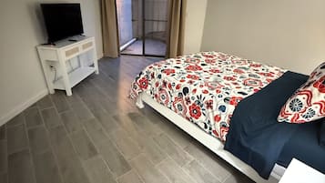 Un dormitorio con cama, televisor en una mesita de noche y puerta corrediza de vidrio que da a un espacio exterior.