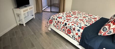 Una camera da letto con un letto, una TV su un comodino e una porta scorrevole in vetro che dà su uno spazio all'aperto.
