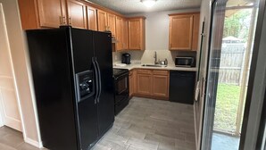 Una cucina con mobili in legno, un frigorifero nero e una porta scorrevole in vetro che dà su un patio.